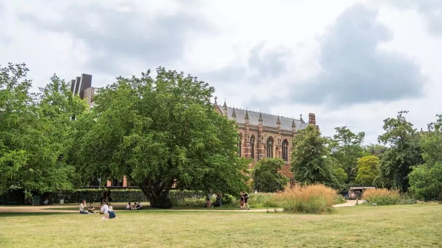Visitors sitting on the grass under the trees at University Parks with Keble College in the background