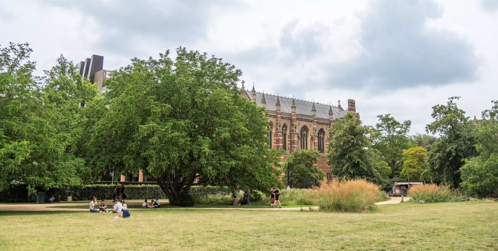 Visitors sitting on the grass under the trees at University Parks with Keble College in the background